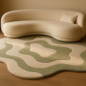 May include: A cream-coloured, curved sofa with a matching cushion sits above a wavy, abstract rug. The rug features a layered design in shades of green and cream, creating a soft, inviting aesthetic. The room has a neutral colour palette.