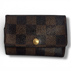 May include: A brown and black checkered wallet with a gold button closure. The wallet is rectangular and has a flap that folds over to close. The pattern is a repeating grid of dark brown and black squares.