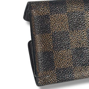May include: Close-up of a black and brown patterned wallet. The wallet has a textured surface with a repeating pattern of dark brown and tan shapes. The edges are black and the wallet appears to be closed.
