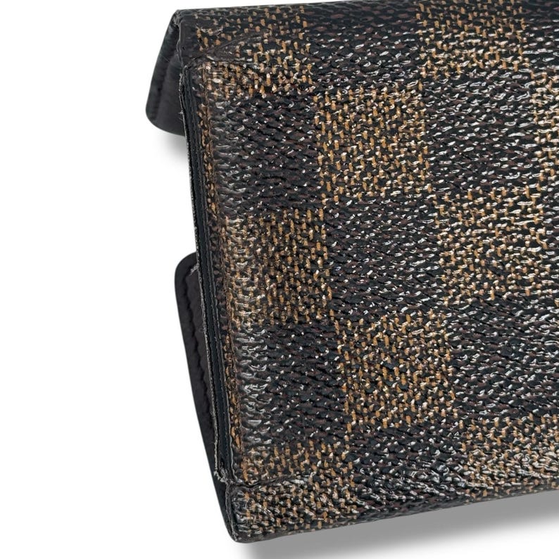 May include: Close-up of a black and brown patterned wallet. The wallet has a textured surface with a repeating pattern of dark brown and tan shapes. The edges are black and the wallet appears to be closed.