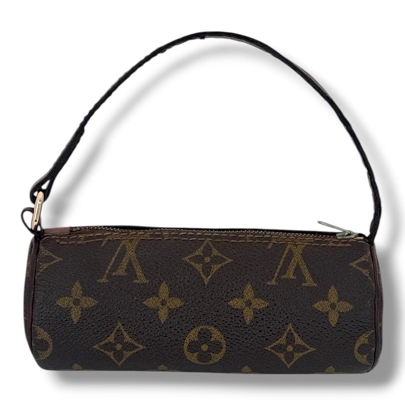 May include: Cylindrical brown and tan handbag with a black handle. The bag has a repeating pattern of interlocking shapes and letters. The silver zip and gold-coloured hardware attach the handle.