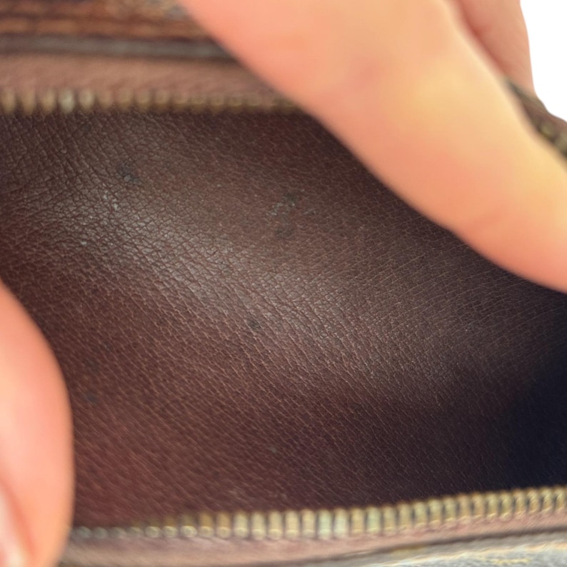 May include: Close-up of the interior of a brown leather wallet. The leather has a textured appearance with visible grain. A zipper is visible at the bottom of the frame, and a hand is partially visible at the top.