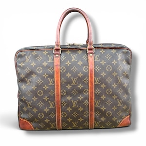 May include: Brown and tan monogrammed briefcase with leather accents. The bag features a repeating pattern of interlocking initials and floral motifs. It has a top handle and two vertical leather straps. The corners and handle are made of brown leather.