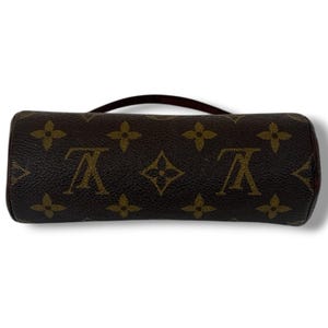 May include: A cylindrical brown handbag with a short handle. The bag features a repeating pattern of brown floral and logo designs. The bag is approximately 15 cm long and 5 cm in diameter.