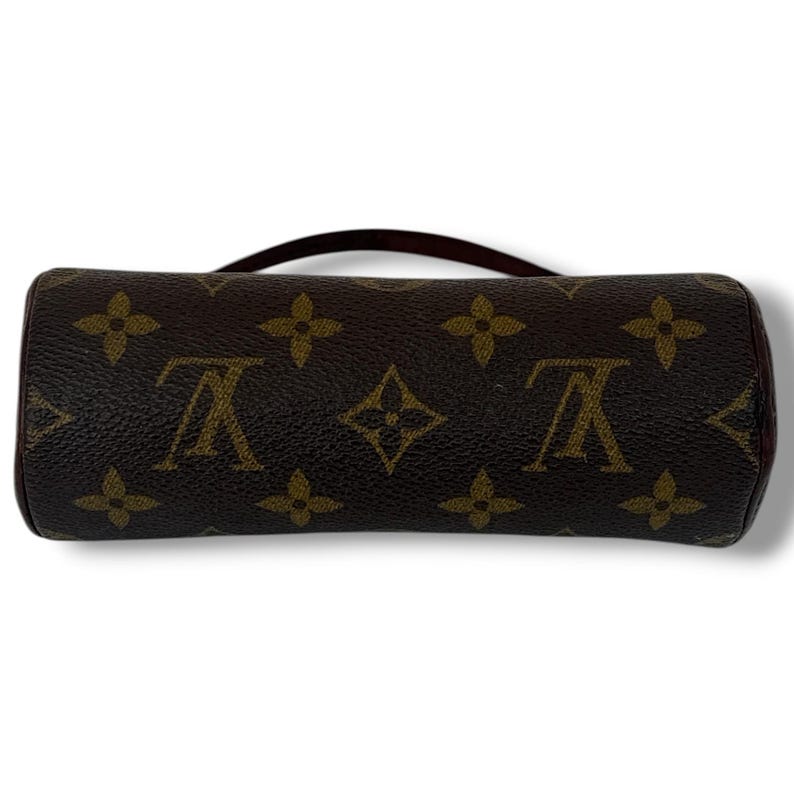 May include: A cylindrical brown handbag with a short handle. The bag features a repeating pattern of brown floral and logo designs. The bag is approximately 15 cm long and 5 cm in diameter.