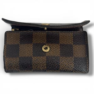 May include: A brown and black checkered pattern key holder with a gold-tone button closure. The key holder is open, revealing the interior. The design is a classic, recognizable pattern.