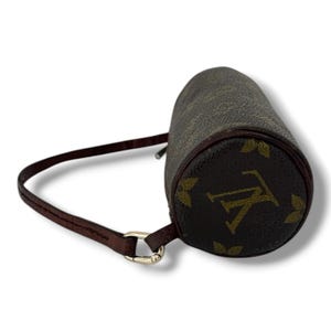 May include: A brown cylindrical handbag with a brown leather strap and gold-coloured hardware. The bag features a repeating pattern of brown and gold logos. The bag is a small size.