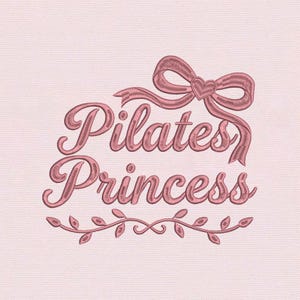 Puede incluir: Diseño bordado en rosa con las palabras "Pilates Princess" en cursiva, coronado por un lazo y un corazón, y un diseño de hojas en la parte inferior. El diseño está sobre una tela rosa claro.
