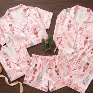 May include: A set of light pink pyjamas featuring a repeating pattern of nutcrackers, bows, Christmas trees, and mugs. The set includes short-sleeved button-down tops, long-sleeved button-down tops, shorts with a tie waist, and long trousers.