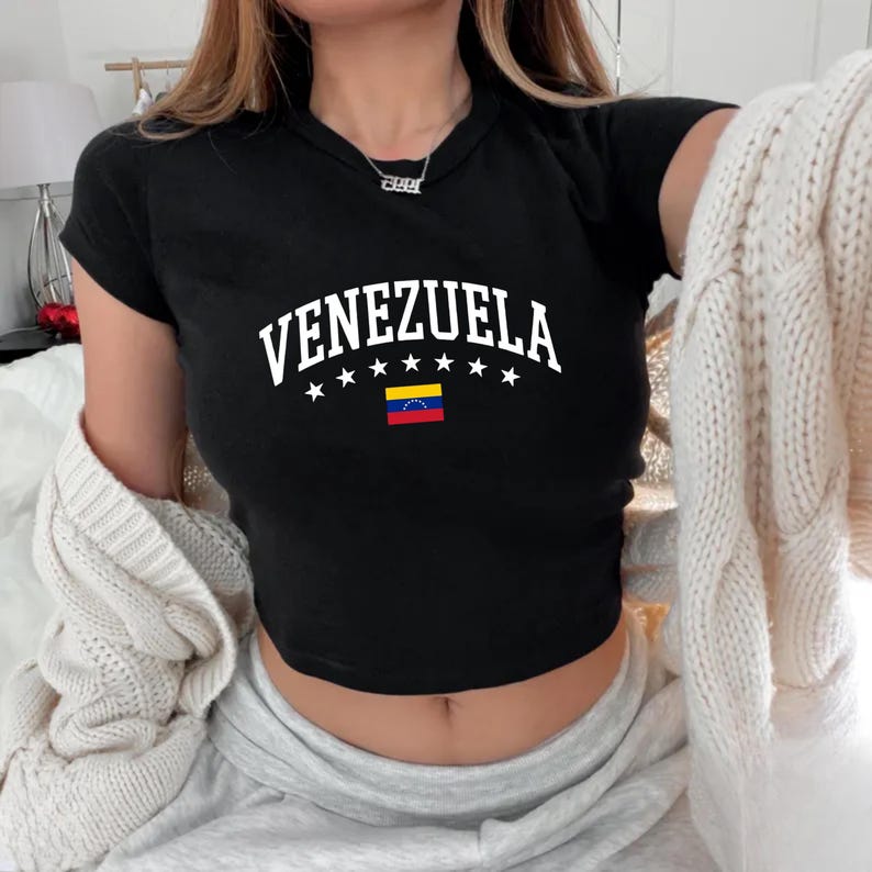 May include: Black crop top with the word "VENEZUELA" in white, arched above a row of white stars and the Venezuelan flag. The shirt has short sleeves and a round neckline.
