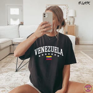 May include: Black t-shirt with the word "VENEZUELA" in white block letters, with white stars above and a small Venezuelan flag below. The word "BLACK" is in the top right corner.