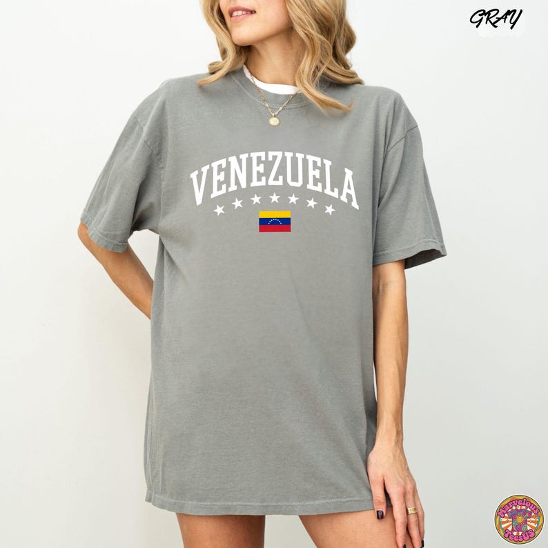 May include: Gray t-shirt with the word "VENEZUELA" in white arched lettering above a small Venezuelan flag. The shirt has a crew neck and short sleeves. The word "GRAY" is printed in the upper right corner.