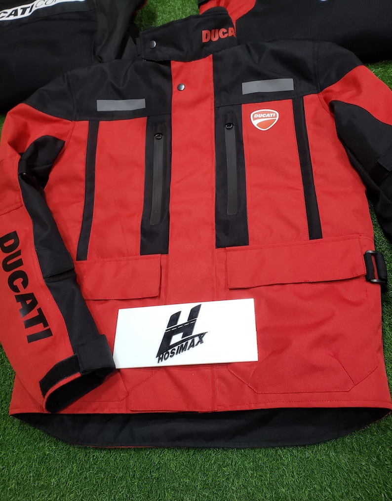 May include: Red and black Ducati motorcycle jacket with the Ducati logo on the chest and sleeve. The jacket has multiple pockets, reflective stripes, and the word "DUCATI" printed on the sleeve. A white sign with the text "HOSIMAX" is in front of the jacket.