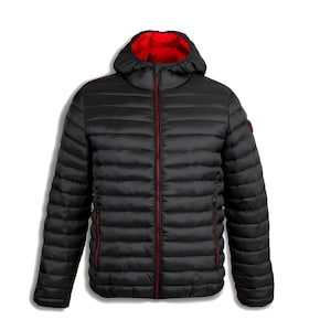 Puede incluir: Una chaqueta acolchada negra con capucha y forro interior rojo. La chaqueta tiene una cremallera roja y un pequeño emblema rojo en la manga superior izquierda. La chaqueta está diseñada con costuras horizontales.
