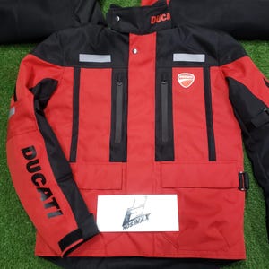 May include: Red and black motorcycle jacket with the Ducati logo on the chest and sleeve. The jacket has a high collar, multiple pockets, and reflective stripes. The word "DUCATI" is printed on the sleeve.