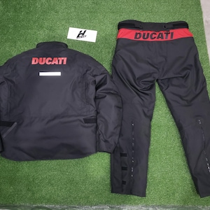 May include: Black Ducati motorcycle jacket and pants set. The jacket has the Ducati logo in red on the back and a white stripe. The pants have a red waistband with the Ducati logo.