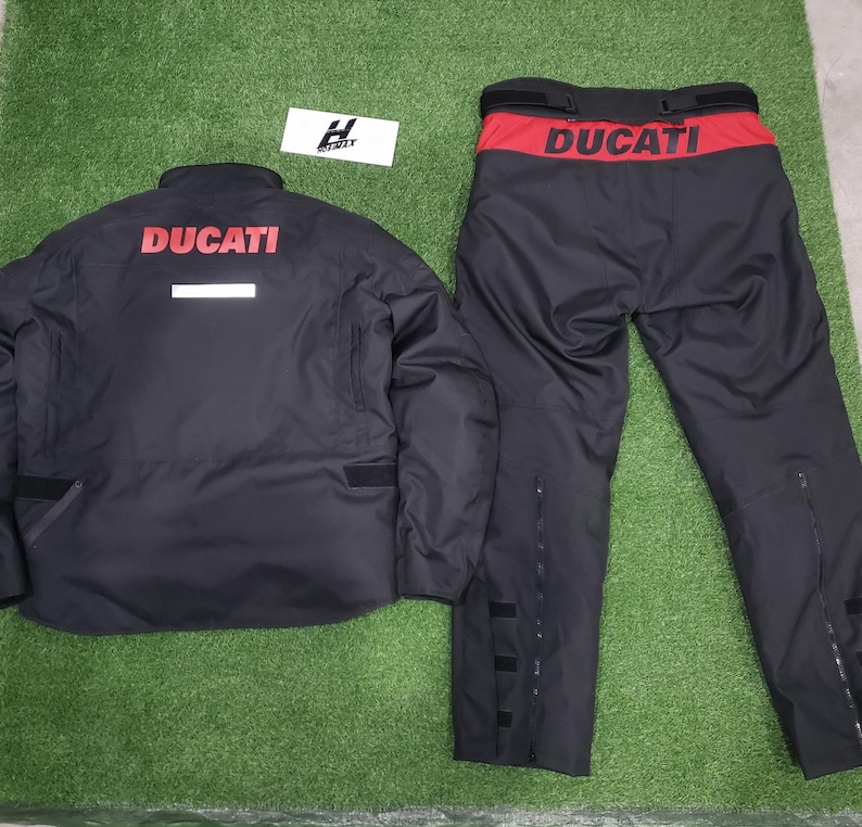 May include: Black Ducati motorcycle jacket and pants set. The jacket has the Ducati logo in red on the back and a white stripe. The pants have a red waistband with the Ducati logo.