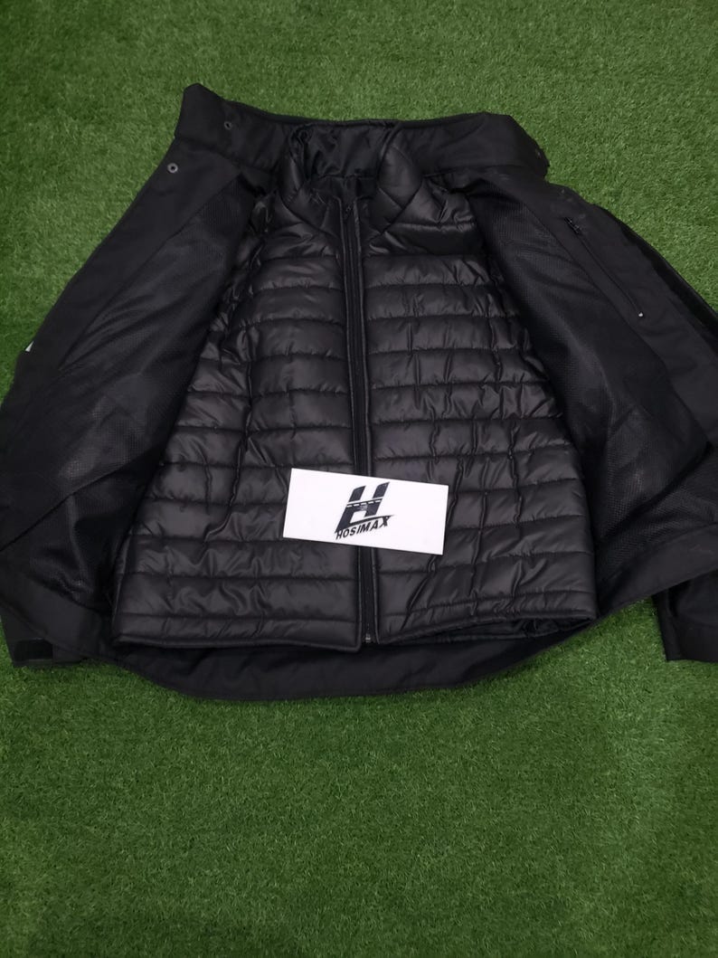 May include: Black jacket with a quilted inner layer, unzipped to reveal the interior. The outer shell has a collar and button closures. A white rectangular tag with the text "HOSIMAX" is visible.