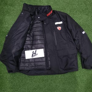 May include: Black motorcycle jacket with the word "DUCATI" in red on the collar. The jacket has a red and white logo on the chest and a removable inner layer. The jacket also has the "HOSIMAX" logo on the inner layer.