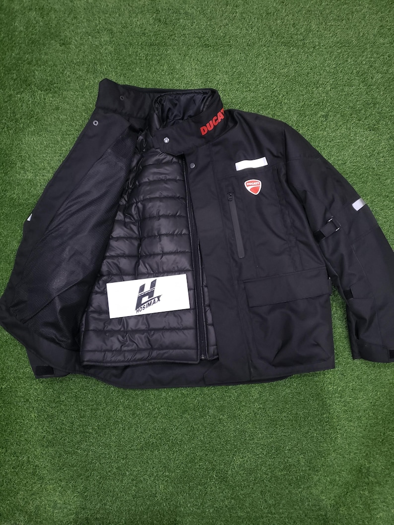 May include: Black motorcycle jacket with the word "DUCATI" in red on the collar. The jacket has a red and white logo on the chest and a removable inner layer. The jacket also has the "HOSIMAX" logo on the inner layer.