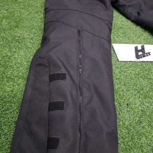 May include: Black jacket with a red stripe across the top, featuring a full-length zipper and three velcro patches. The jacket is made of a durable material and has the brand name "HOSIMAX" on a white label.