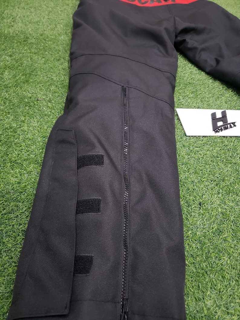 May include: Black jacket with a red stripe across the top, featuring a full-length zipper and three velcro patches. The jacket is made of a durable material and has the brand name "HOSIMAX" on a white label.