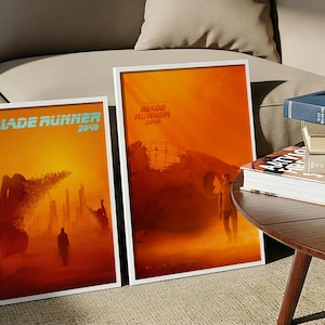 May include: Two framed posters with white borders, featuring artwork from "Blade Runner 2049." The posters have a warm color palette of orange and red, with silhouettes of figures and futuristic cityscapes. The text "Blade Runner 2049" is visible.