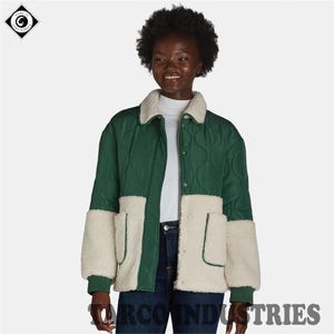 May include: A green and cream quilted jacket with a cream shearling collar and pocket details. The jacket features a zip-up front. The brand name "TARCO INDUSTRIES" is printed at the bottom. The jacket is worn by a person.
