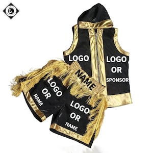 Op de afbeelding: Een zwart en goudkleurige boksset bestaande uit een mouwloos vest met capuchon en ritssluiting en een bijpassende broek. Het vest heeft gouden biezen, de broek is versierd met gouden franjes en beide delen bevatten witte tekst: LOGO, NAME of SPONSOR.