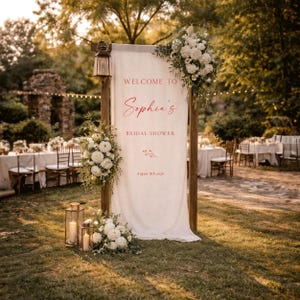May include: A wooden sign with a white fabric banner, decorated with flowers and candles. The sign says "Welcome to Sophia's Bridal Shower, August 8th 2026." The scene is set outdoors with tables and chairs, creating a celebratory atmosphere.