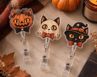 Peut inclure: Trois enrouleurs de badge en acrylique avec des motifs de chats sur le thème d'Halloween. Celui de gauche montre un chat dans une citrouille, celui du centre un chat en fantôme, et celui de droite un chat noir avec un chapeau de sorcière.