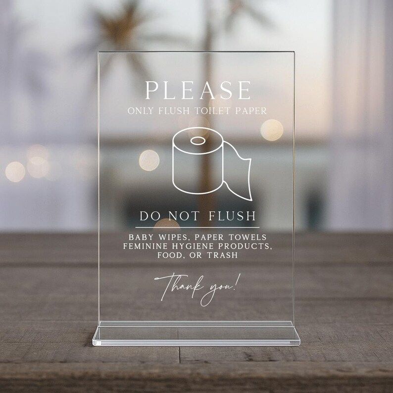 May include: A clear acrylic sign with white text and a toilet paper roll graphic. The sign reads "PLEASE ONLY FLUSH TOILET PAPER" and "DO NOT FLUSH" with a list of items not to flush. The sign ends with "Thank you!"
