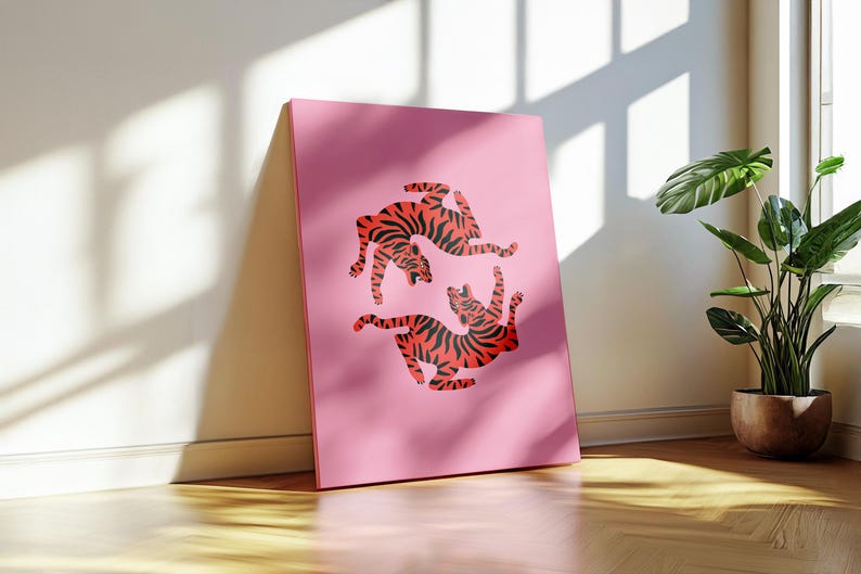 K&ouml;nnte beinhalten: Ein pinkfarbener Leinwanddruck mit zwei roten Tigern mit schwarzen Streifen in einer dynamischen Pose. Das Kunstwerk steht vor einer Wand in einem gut beleuchteten Raum. Der Hintergrund ist einfarbig pink.