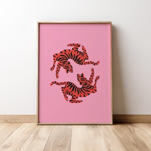 K&ouml;nnte beinhalten: Ein gerahmter Kunstdruck mit zwei stilisierten Tigern in einer spielerischen Pose. Die Tiger sind orange mit schwarzen Streifen, vor einem leuchtend rosa Hintergrund. Der Rahmen ist goldfarben und verleiht einen Hauch von Eleganz.