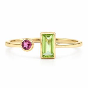 May include: A gold open-style ring featuring a round, bezel-set pink gemstone on one end and a rectangular, baguette-cut light green gemstone on the other. The band is smooth and polished, creating a delicate and balanced design with two distinct stones.