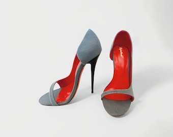 May include: A pair of light blue denim high-heeled sandals featuring a pointed-toe silhouette, a thin stiletto heel, and a vibrant red interior lining. The shoes have an open-toe design with a single strap across the front and a closed heel counter.