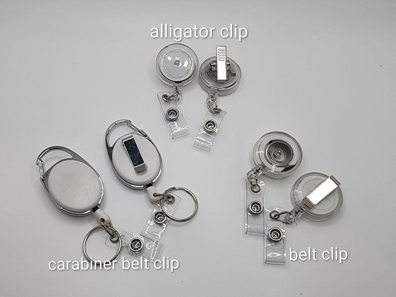 May include: A collection of clear plastic badge reels with various clip styles, including alligator clips, carabiner belt clips, and belt clips. The text "alligator clip", "carabiner belt clip", and "belt clip" are visible.