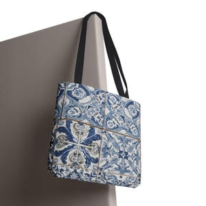 May include: Tote bag featuring a blue and white tile pattern. The bag has black straps and a rectangular shape. The tile design includes floral and geometric elements in shades of blue and white.