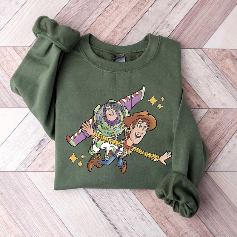 Może przedstawiać: Zielona bluza z grafiką Buzza Astrala i Chudego z Toy Story. Postacie z kresk&oacute;wek są przedstawione w powietrzu z gwiezdnym tłem. Bluza ma długie rękawy i okrągły dekolt.