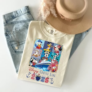 May include: Cream-colored t-shirt featuring a Disney Cruise Line graphic with Mickey Mouse, Donald Duck, and other characters. The shirt is paired with light-wash jeans, a necklace, and a tan hat. The graphic includes the text "2023" and "2025".