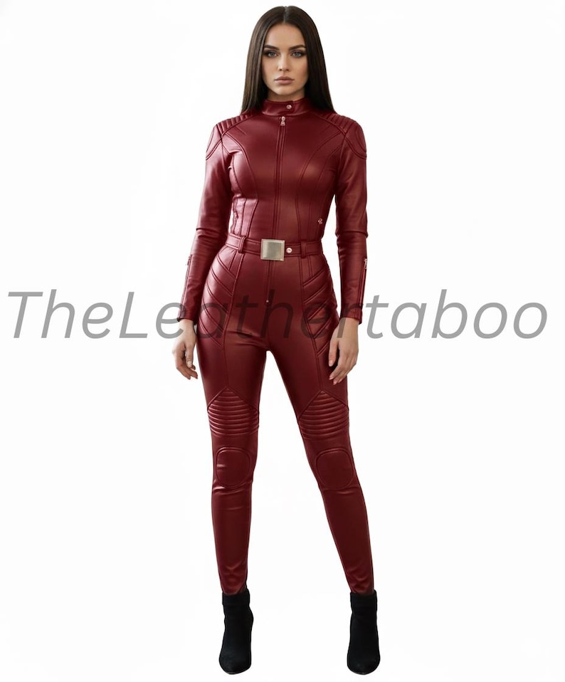 May include: A burgundy leather jumpsuit with a high collar, long sleeves, and a front zipper. The jumpsuit features a belt with a silver buckle and quilted detailing on the shoulders and legs. The text "TheLeatherTaboo" is visible.