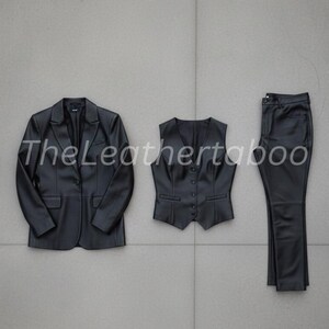 May include: A three-piece black leather suit set, including a blazer, vest, and pants. The blazer has a two-button closure, the vest has a button-down front, and the pants are straight-legged. The set is displayed on a gray tiled surface.
