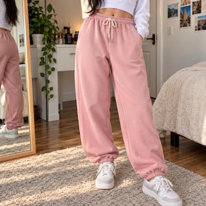 Könnte beinhalten: Altrosa Jogginghose mit hoch sitzendem elastischem Bund, funktionalem cremefarbenem Kordelzug, Seitentaschen und elastischen Beinabschlüssen. Die Hose hat eine lockere, weit geschnittene Passform und besteht aus Stoff.