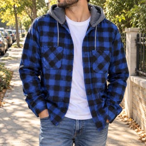 May include: A long-sleeve button-up shirt featuring a blue and black buffalo plaid pattern, a gray jersey hood with matching drawstrings, and two chest pockets. The shirt is worn over a plain white t-shirt and paired with blue denim jeans.