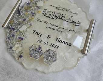 Könnte beinhalten: Ein dekoratives Tablett mit silbernen Griffen, das ein weißes und silbernes Harzdesign mit getrockneten Blumen und Text aufweist. Das Tablett enthält die Namen "Faiz & Hanna" und das Datum "06.07.2024" sowie ein Zitat aus dem Koran.