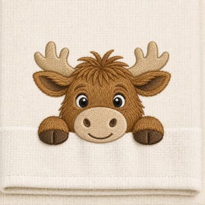 May include: A cream-colored hand towel featuring an embroidered design of a brown Highland cow calf with tan antlers. The cow is positioned as if peeking over the folded edge of the towel, displaying a detailed face with dark eyes and hooves.