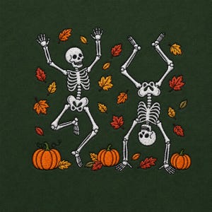 May include: An embroidered design on a dark green fabric featuring two white skeletons in playful poses surrounded by scattered orange, red, and yellow autumn leaves. Three orange pumpkins are positioned along the bottom of the embroidery.