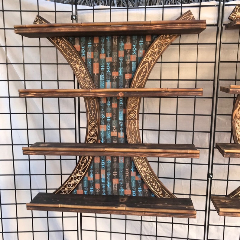 Puede incluir: Estanter&iacute;a de madera de tres niveles con un dise&ntilde;o tallado y un patr&oacute;n geom&eacute;trico en azul, naranja y negro. La estanter&iacute;a est&aacute; hecha de madera oscura y tiene un aspecto r&uacute;stico.