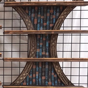 Puede incluir: Una estanter&iacute;a de madera con tres estantes. Los estantes son curvos y tienen un dise&ntilde;o decorativo en la parte delantera. El dise&ntilde;o es un patr&oacute;n geom&eacute;trico azul oscuro y marr&oacute;n. Los estantes est&aacute;n montados en una rejilla de alambre negro.