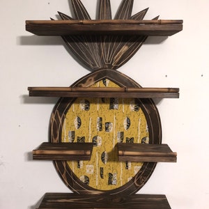May include: A wooden pineapple-shaped shelf unit with three shelves. The shelves are made of dark wood with a light wood trim. The pineapple is decorated with a yellow and black patterned fabric.